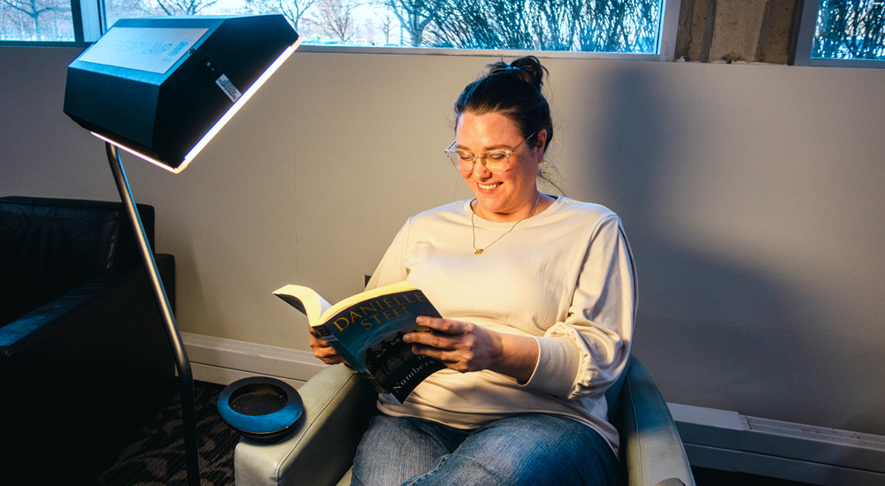 adult reading a book sitting behind a light therapy lamp